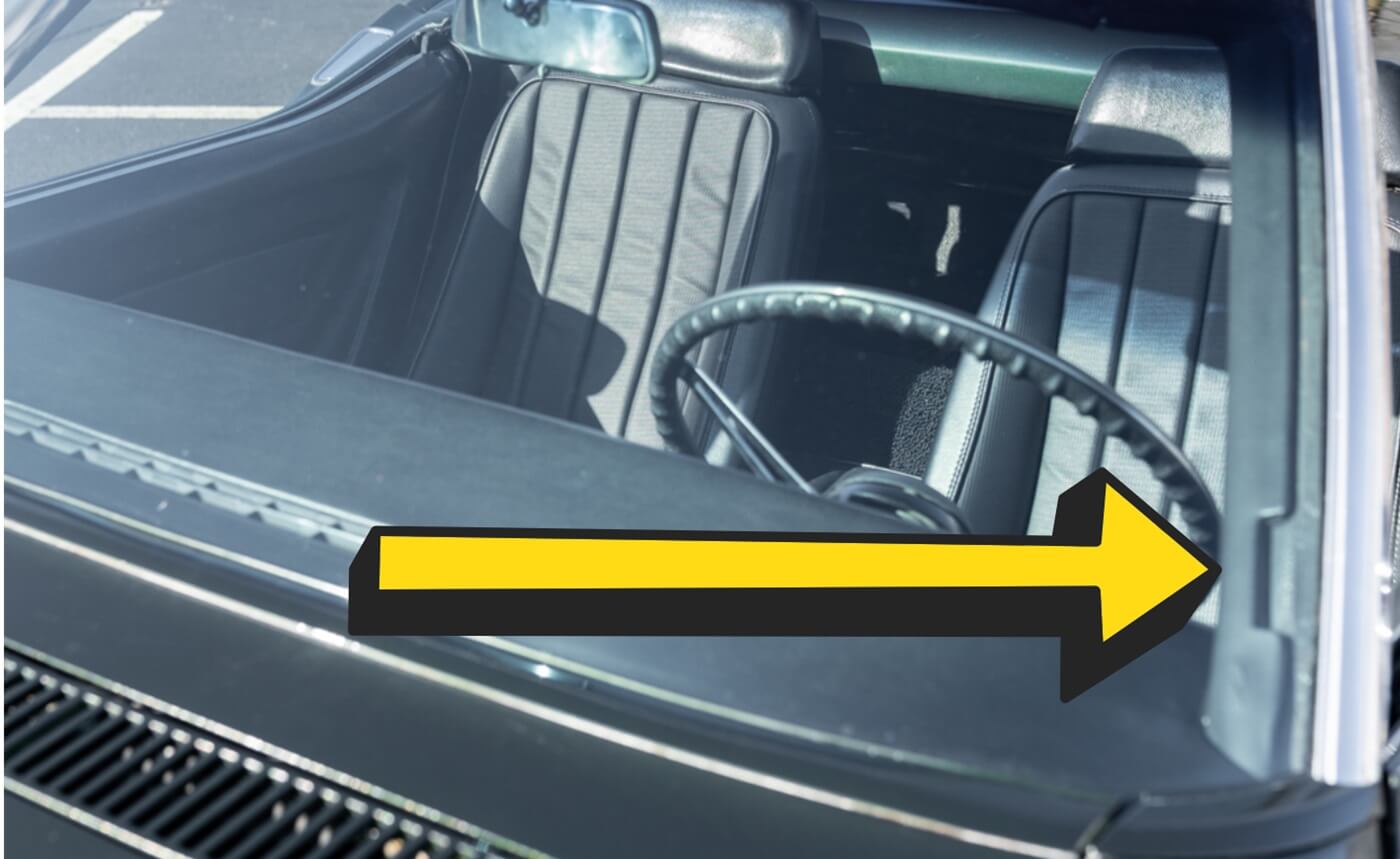 A close-up image of a Corvette C3 VIN plate, riveted to the bottom front face of the driver's side windshield pillar. The VIN is visible through the glass.